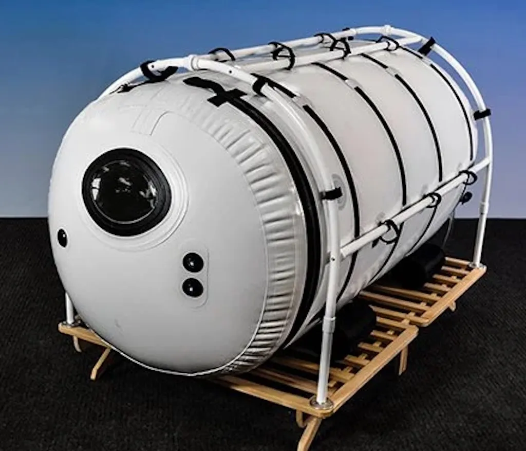 The Grand Dive Pro, a large white Summit to Sea chamber with a round window, on a raised wooden platform.